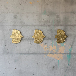 KIFF KIFF Amal gold hammered metal dove ex-voto wall decorations arranged in a row on a grey concrete wall