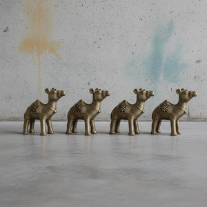 Four KIFF KIFF brass dromedary statuettes with intricate textured detailing arranged in a row on a concrete surface.
