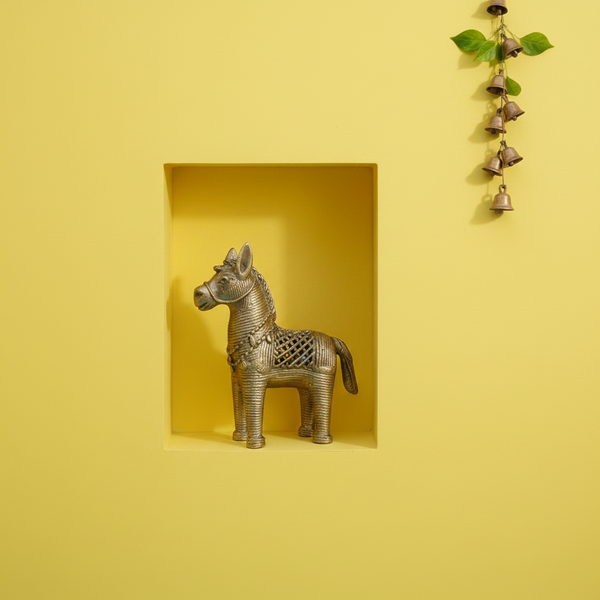 KIFF KIFF brass horse statuette with intricate filigree details displayed in a yellow wall niche with hanging bells