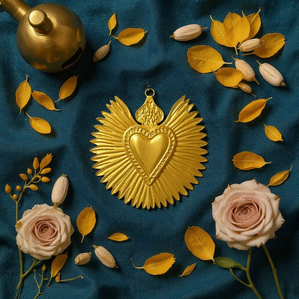 Ex-voto Cléo KIFF KIFF en métal doré en forme de cœur rayonnant, posé sur un tissu bleu avec des fleurs et feuilles.