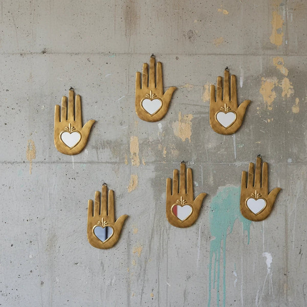 Composition murale de six ex-voto KIFF KIFF en forme de main stylisée en métal doré avec un cœur central miroir