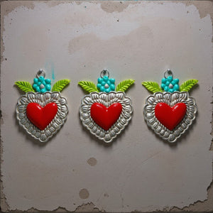 Trois ex-voto KIFF KIFF modèle Trixie en métal argenté ciselé avec cœur rouge, fleur turquoise et feuilles vert lime