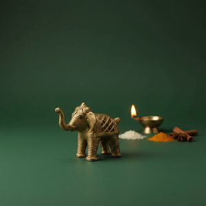 KIFF KIFF gold metal elephant figurine with intricate textured engravings on a dark green background with a diya lamp.