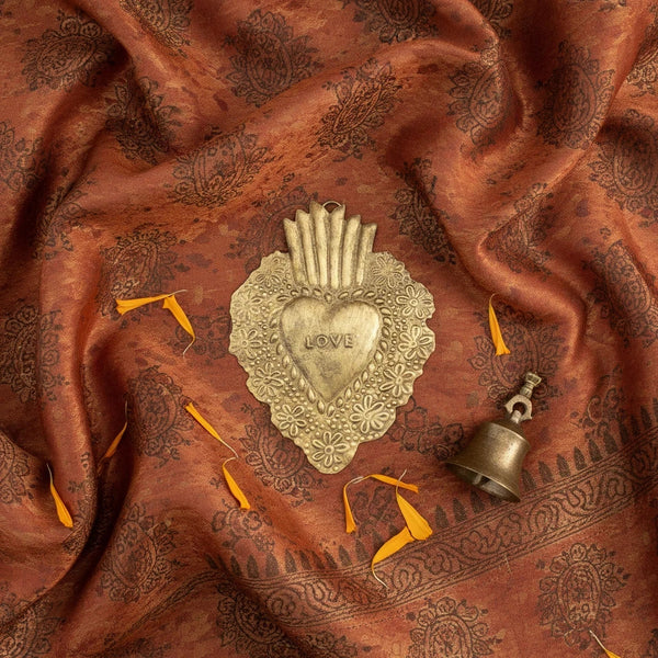 KIFF KIFF Freddy gold metal heart ex-voto with LOVE inscription, handcrafted in India, on a patterned brown fabric.