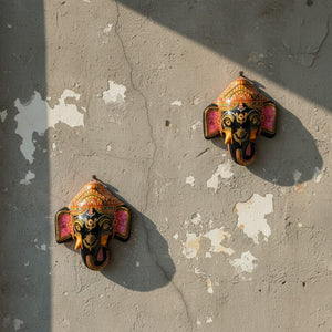 Deux masques muraux Ganesh KIFF KIFF en papier mâché noir avec détails peints à la main, fixés sur un mur texturé.