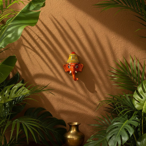 Masque mural Ganesh Vinayaka rouge en papier mâché artisanal KIFF KIFF sur un mur texturé entouré de plantes tropicales
