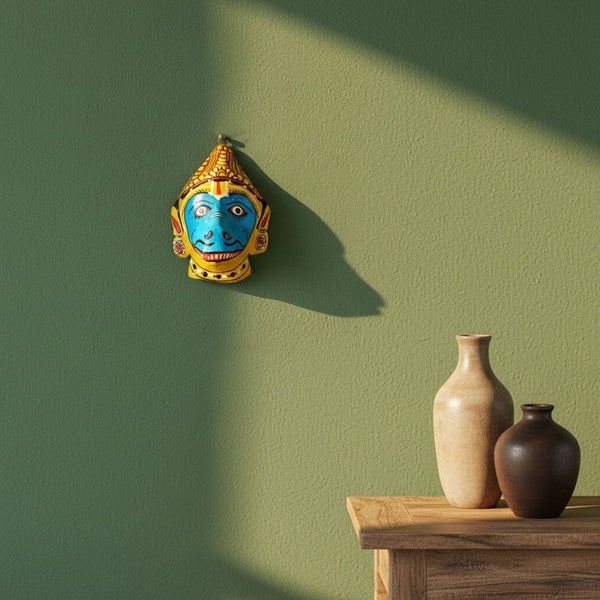 Masque mural artisanal KIFF KIFF Jambaban en papier mâché jaune et bleu suspendu sur un mur vert