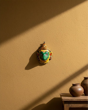Masque mural artisanal KIFF KIFF Jambaban en papier mâché jaune et vert, suspendu sur un mur ocre