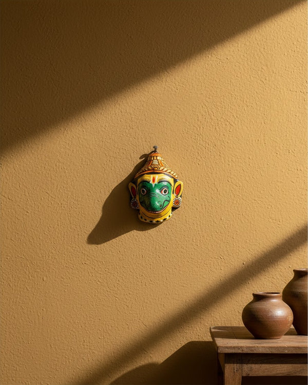 Masque mural artisanal KIFF KIFF Jambaban en papier mâché jaune et vert, suspendu sur un mur ocre