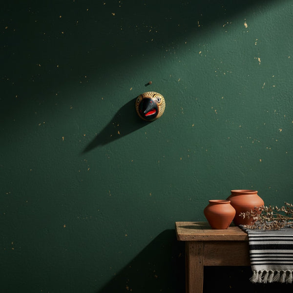 Masque mural KIFF KIFF Jatayu en papier mâché jaune et noir suspendu sur un mur vert sombre au-dessus d'une table