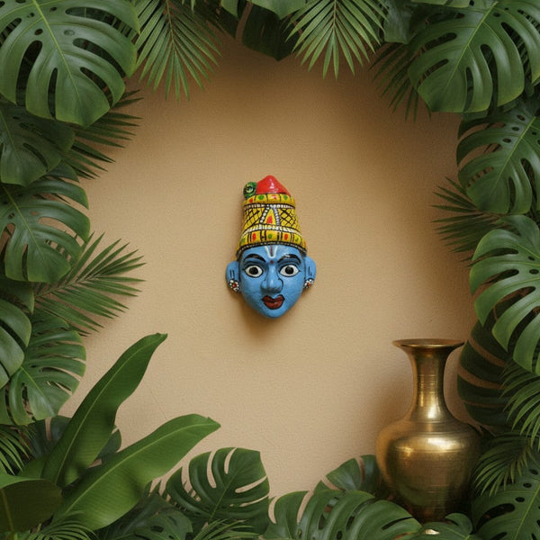 Masque mural artisanal KIFF KIFF de Radha en papier mâché bleu, peint à la main, entouré de feuilles tropicales