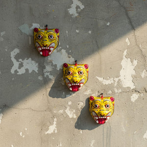 Trois masques muraux KIFF KIFF en papier mâché jaune représentant des tigres artisanaux d'Inde fixés sur un mur gris.