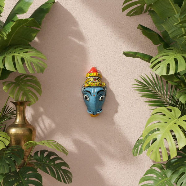 Masque mural artisanal KIFF KIFF de Varaha en papier mâché peint à la main, 10 cm, sur un mur rose avec des plantes.