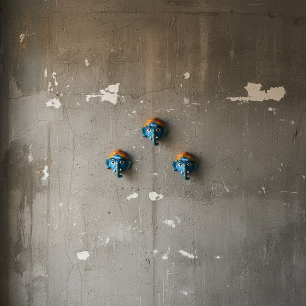 Trois masques muraux artisanaux KIFF KIFF représentant Ganesh en papier mâché bleu sur un mur en béton brut.