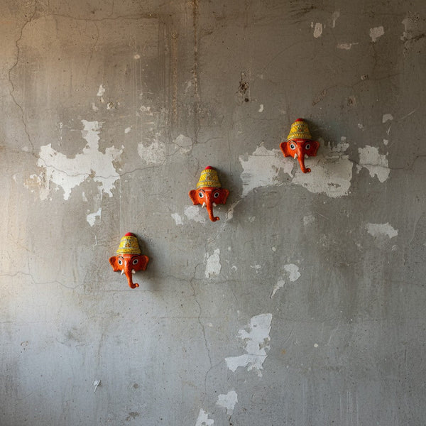 Trois masques muraux KIFF KIFF Ganesh Vinayaka en papier mâché rouge peints à la main sur un mur en béton brut