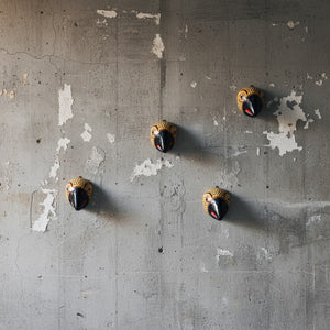 Quatre masques muraux KIFF KIFF Jatayu en papier mâché jaune moutarde et bec noir sur un mur en béton brut.