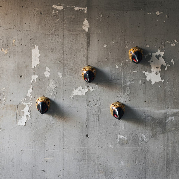 Quatre masques muraux KIFF KIFF Jatayu en papier mâché jaune moutarde et bec noir sur un mur en béton brut.