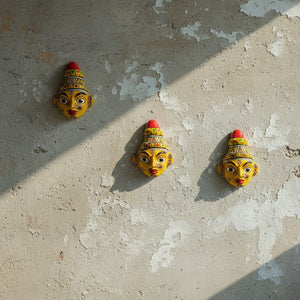 Trois masques muraux artisanaux KIFF KIFF représentant le visage jaune de Krishna en papier mâché sur un mur texturé