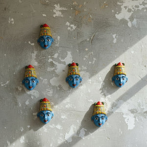 KIFF KIFF petits masques muraux artisanaux de Radha en papier mâché bleu, peints à la main, disposés sur un mur gris.