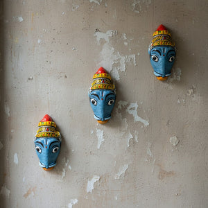 Trois masques muraux artisanaux KIFF KIFF de Varaha en papier mâché peint à la main, fixés sur un mur texturé.