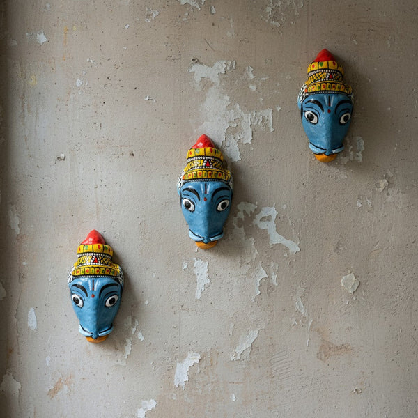 Trois masques muraux artisanaux KIFF KIFF de Varaha en papier mâché peint à la main, fixés sur un mur texturé.
