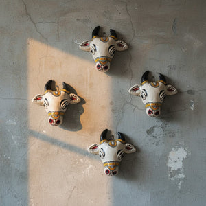 Quatre mini masques KIFF KIFF de vaches sacrées blanches en papier mâché, décorés à la main, fixés sur un mur gris.