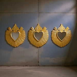 Trois miroirs ex-voto dorés KIFF KIFF modèle Finch en forme de cœur avec rayons ciselés sur un mur gris