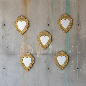 Composition murale de cinq miroirs ex-voto KIFF KIFF en métal doré martelé en forme de cœur sur un mur en béton