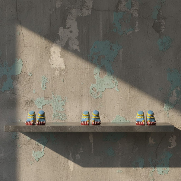 Trois paires de pieds de Lakshmi KIFF KIFF en papier mâché bleu, posées sur une étagère devant un mur texturé.