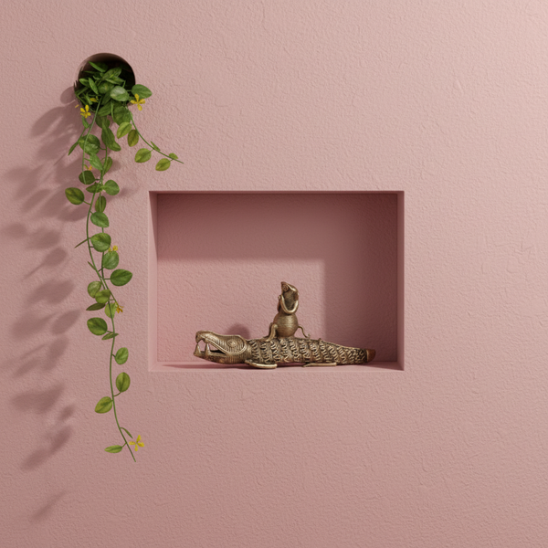 Statuette crocodile KIFF KIFF en laiton doré posée dans une niche murale rose avec une plante tombante